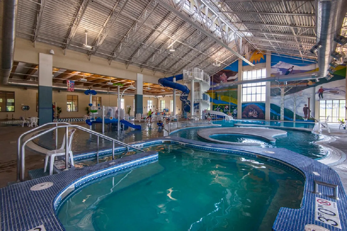 A lively, colorful interior shot of the Grand Park Rec Center pool area, with water slides, children playing, and vibrant decor. The energy conveys family fun and recreational opportunities.