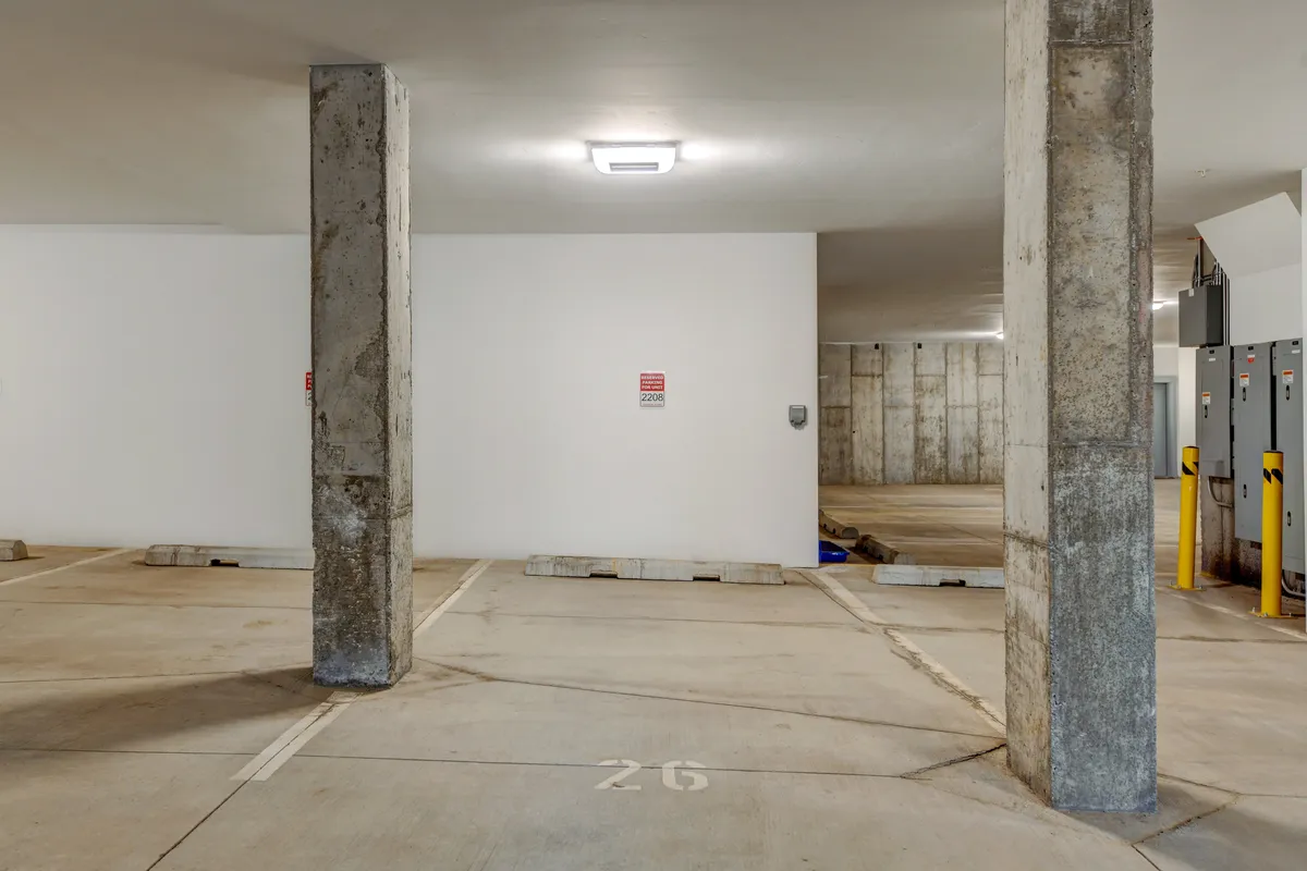 This image captures the underground parking area, featuring concrete pillars, marked parking spaces, and bright lighting fixtures. The environment is utilitarian and clearly designed for vehicle storage and easy access to the building’s living spaces.