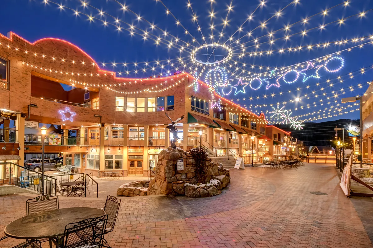 A lively outdoor area with twinkling string lights, decorative stars, a charming stone fountain, and inviting seating. The ambience is festive and social, ideal for enjoying downtown entertainment and seasonal events.