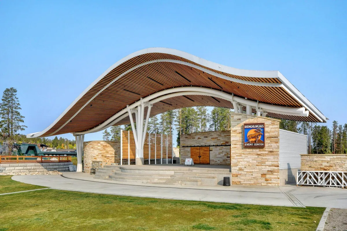 A striking exterior shot of the Hideaway Park amphitheater, showing its curved roof, stone facade, and prominent event signage. The space is set for community gatherings, outdoor performances, and seasonal celebrations, reflecting a lively neighborhood hub.