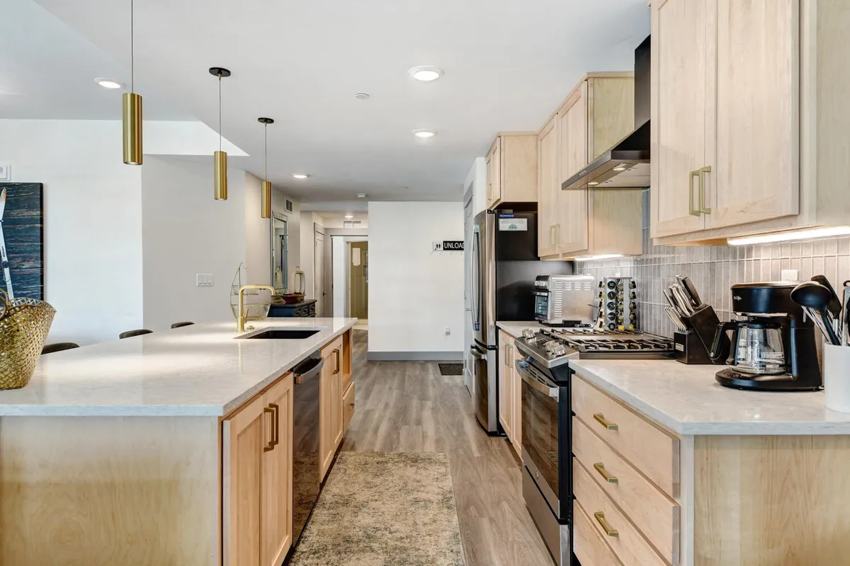 A warm, functional kitchen space featuring a large island counter, stainless steel appliances, wooden cabinetry, and modern light fixtures. The environment is perfect for both culinary endeavors and social gatherings.