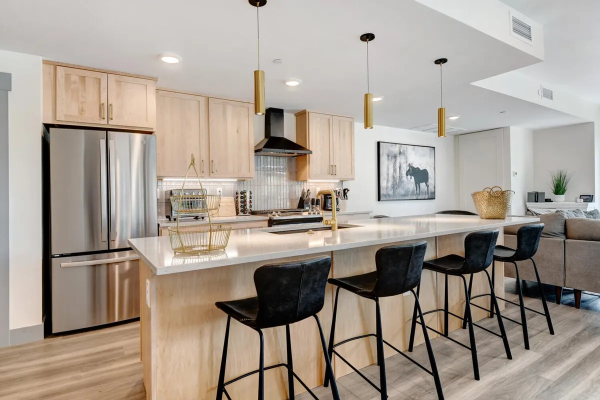 The image showcases a beautifully designed, open-concept kitchen and living space featuring a spacious island countertop with plush seating, sleek modern appliances, and tasteful artwork. The inviting layout is perfect for cooking, entertaining, and gathering with friends and family, all set in a warm, welcoming ambiance.